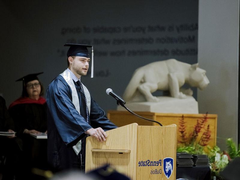 在毕业典礼上，一名身穿长袍、头戴礼帽的男学生正在演讲.