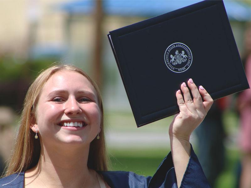 宾州州立大学的毕业生在户外拿着文凭微笑