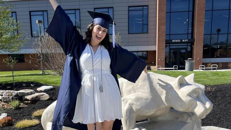 New Penn State graduate Anna Raffeinner celebrates with a joyful expression with the Lion Shrine on the Penn State DuBois campus, just outside the PAW Center
